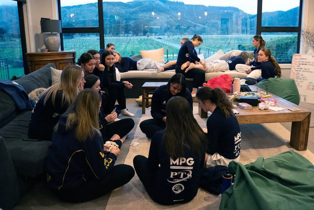 Members of a girls school hockey team playing cards together on the floor while others have massages while staying at Kiwiesque.
