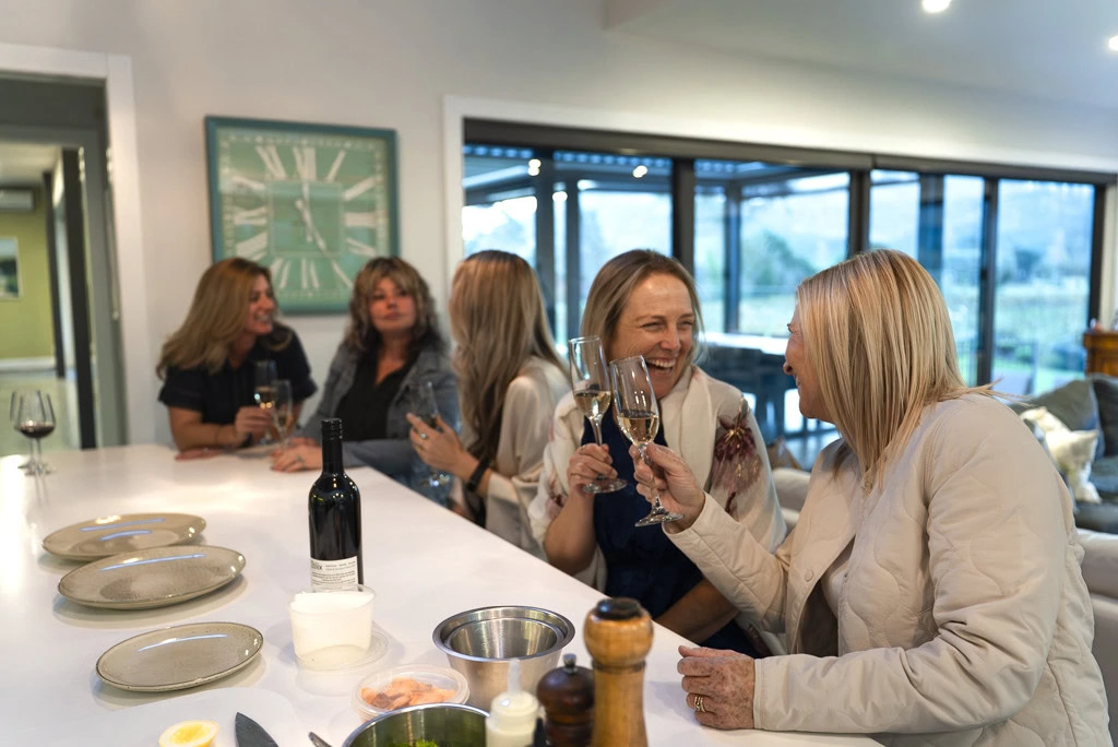 Female guests in conversation at the kitchen bar while holding wine glasses at a Kiwiesque Winter Food and Wine Experience