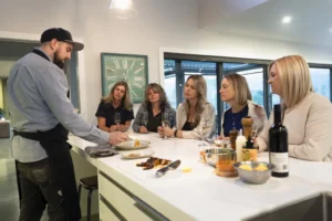 Chef Simon Lillico plating a dish in front of a group of female guests at a Kiwiesque Winter Food and Wine Experience