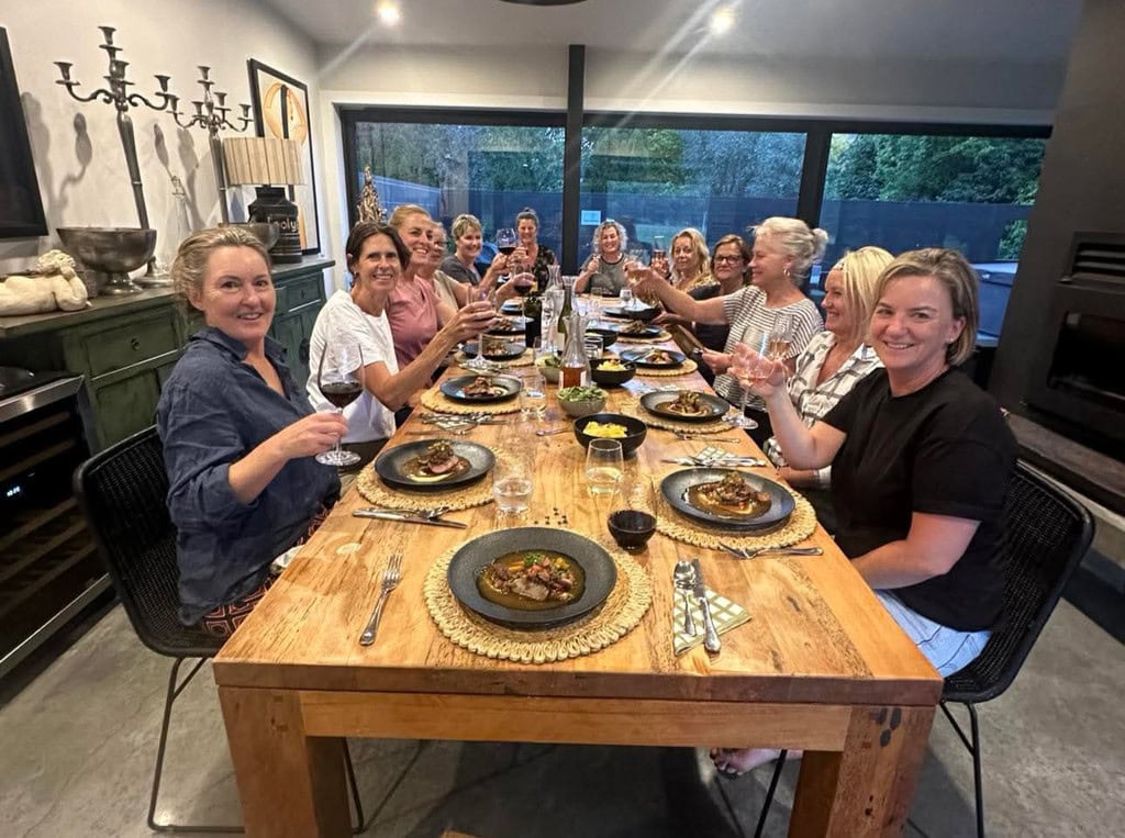 A group of women sitting at a long dining table in the Luxury Lodge at Kiwiesque toasting before starting their dinner